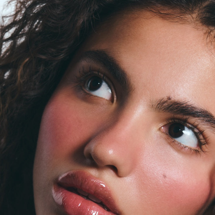 Model wearing Pocket Blush in Teacup, a glowy pink cream blush on cheeks and lips for a dewy, satiny finish.