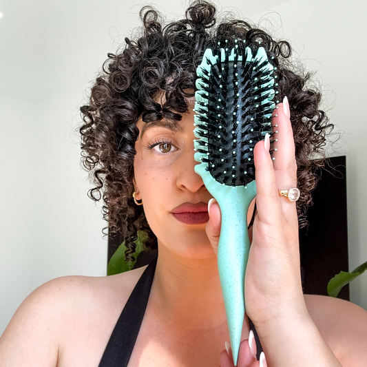 Woman with defined curls holding the mint green CurlPro styling brush for natural wave and curl definition.