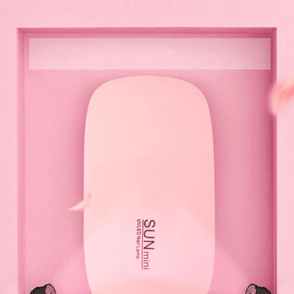 Pink SunMini portable UV LED nail dryer and manicure lamp for curing gel polish on a pink background.
