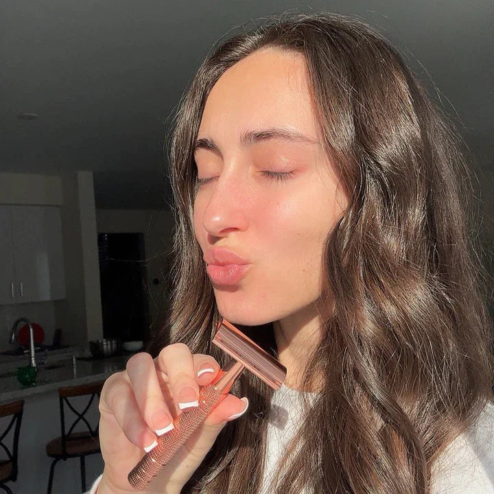 Woman holding the rose gold SmoothShave eco-friendly safety razor with a textured brass handle near her face.