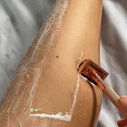 SmoothShave rose gold safety razor with textured brass handle gliding through shaving cream on a woman's leg.