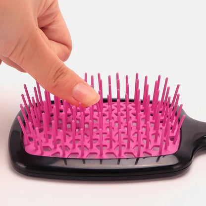 Finger pressing flexible pink bristles on a Silqé black detangling paddle hairbrush to show painless knot removal.